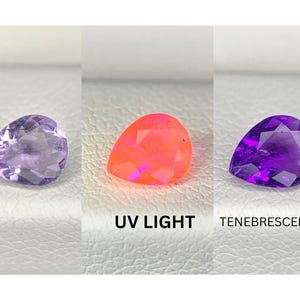 May include: Three pear-shaped gemstones in varying colors. The left gem is light purple, the center gem is bright orange, and the right gem is dark purple. Text below the gems reads "UV LIGHT" and "TENEBRESCENCE".
