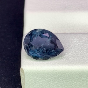 Könnte beinhalten: Ein birnenförmiger Edelstein mit einer Farbpalette aus tiefem Blau und dunklem Türkis. Der Stein weist eine facettierte Oberfläche auf, die das Licht reflektiert und ein komplexes Muster aus hellen und dunklen Blautönen erzeugt.