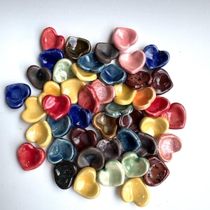 May include: A collection of small heart-shaped ceramic dishes in various colors, including red, blue, yellow, green, and brown. The dishes are perfect for holding small trinkets or serving snacks.