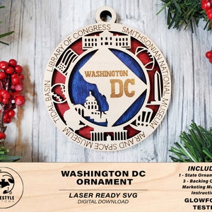 Pode incluir: Ornamento de madeira cortado a laser que representa um mapa de Washington DC com marcos como o Monumento a Washington, o Capitólio e o Museu Nacional do Ar e do Espaço. O ornamento é pintado nas cores vermelho, branco e azul. O texto "WASHINGTON DC" está escrito em dourado no ornamento.