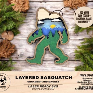 May include: Layered wooden Sasquatch ornament and magnet with a mountain scene inside. The ornament is green and brown with a beige background. The text "Layered Sasquatch Ornament and Magnet" is at the bottom of the image. The text "Laser Ready SVG Digital Download" is below that. The text "Includes 1 Ornament 1 Magnet Marketing Materials Instructions Glowforge & Lightburn Tested!" is on the right side of the image.