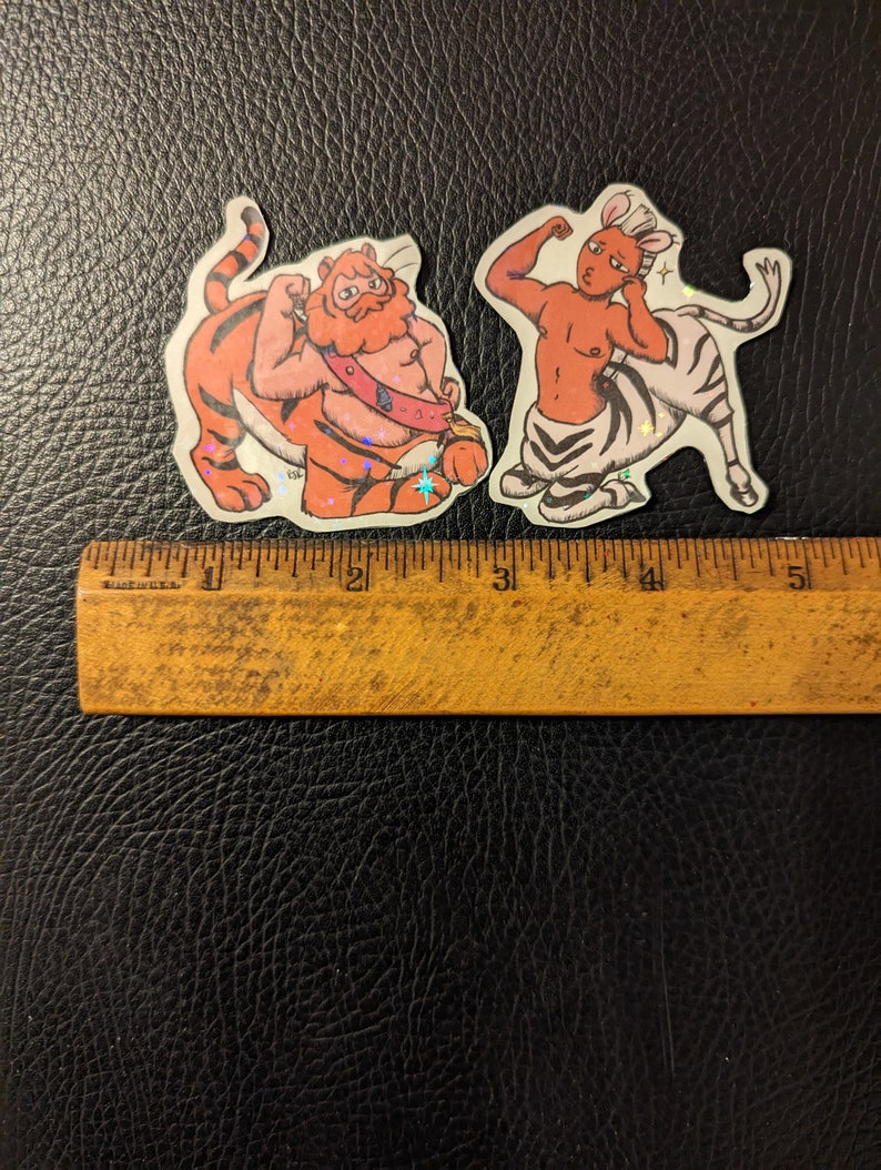 May include: Two colorful stickers featuring a tiger and a zebra with human-like bodies. The tiger is orange and black with a red mane and a blue sash. The zebra is white and black with a pink mane and a blue tail.