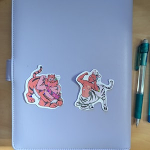 May include: Two colorful stickers featuring anthropomorphic animal characters. The first sticker is a tiger with orange and black stripes, wearing a red and white sash. The second sticker is a zebra with black and white stripes, wearing a red sash and a crown.