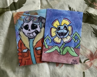 May include: Two watercolour illustrations on white cardstock. The first illustration is of a blue and white skeleton wearing a red and blue jacket with a yellow fur collar and goggles. The second illustration is of a yellow flower with a blue face and a long tongue. The flower has green stems and leaves. The text "RJR 2/13/17" is written in black ink in the bottom right corner of the second illustration.