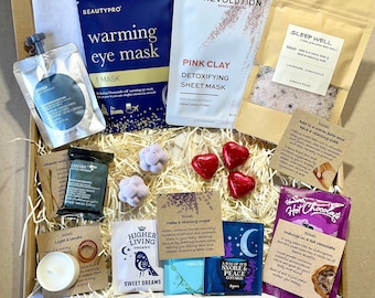 May include: A gift box filled with self-care items, including a pink clay detoxifying sheet mask, a warming eye mask, bath salts, bath bombs, tea bags, hot chocolate, and a candle. The box is filled with shredded paper and has a card that says "Especially for you".