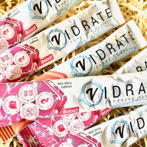 May include: Multiple Vidrate Enhanced Hydration stick packs in mixed berry and original flavours. The packaging features white and pink designs with text including With 30mg Caffeine, Zero Sugar, Suitable for Vegans, and Added Vitamins B5 B6.