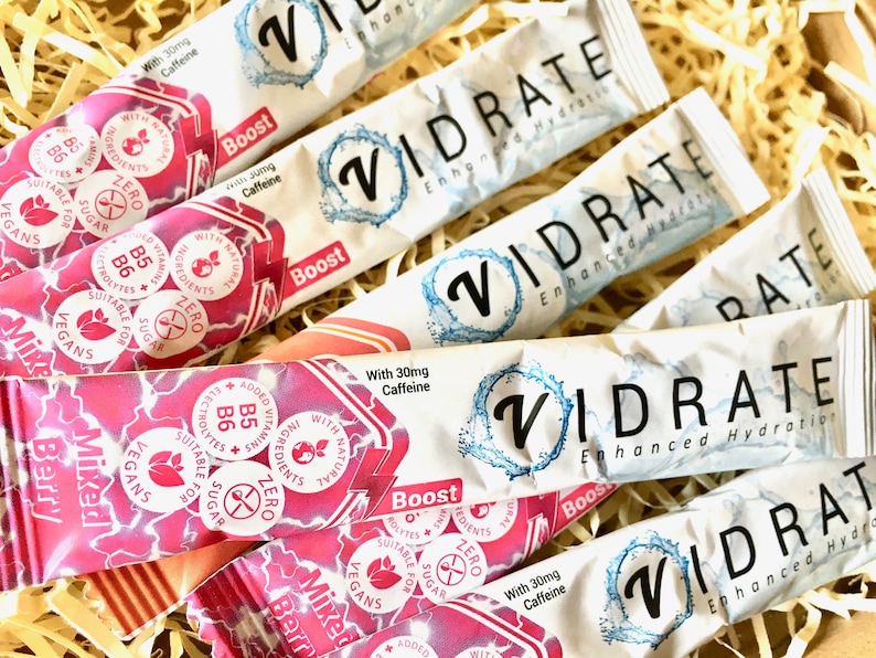 May include: Multiple Vidrate Enhanced Hydration stick packs in mixed berry and original flavours. The packaging features white and pink designs with text including With 30mg Caffeine, Zero Sugar, Suitable for Vegans, and Added Vitamins B5 B6.
