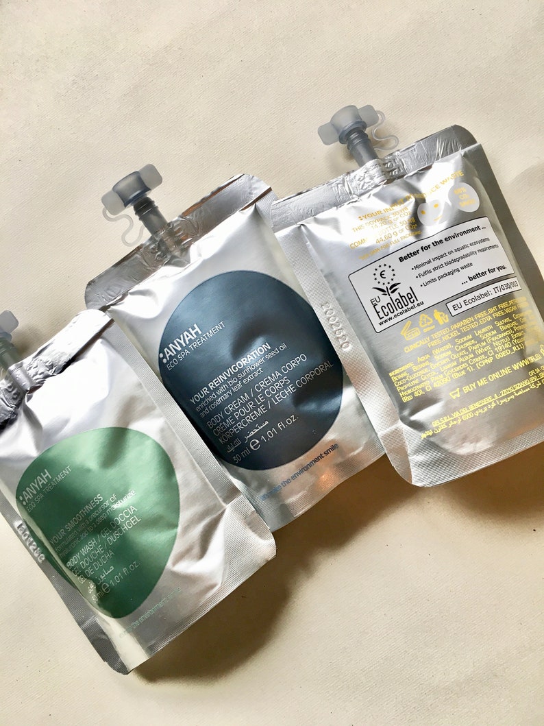 May include: Three silver pouches with blue and green labels. The labels contain text in English and Arabic. The pouches are labeled "Anyah Eco Spa Treatment" and contain body care products. The pouches are 1.01 fluid ounces each.