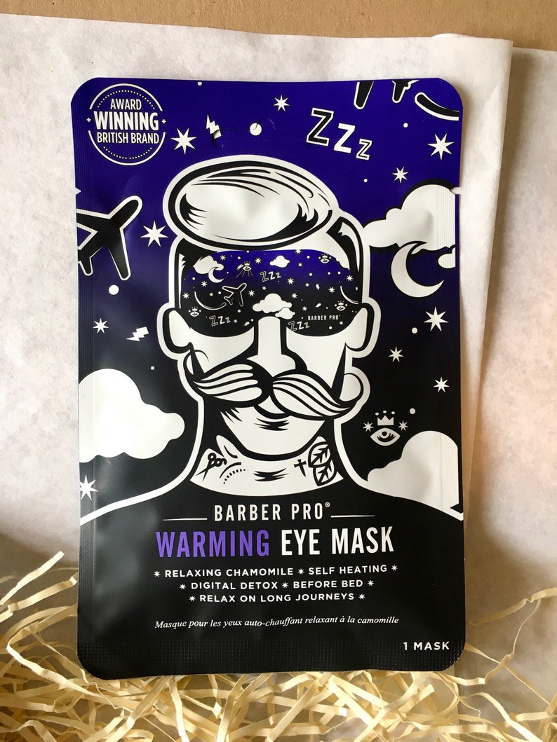 May include: A black eye mask with a cartoon illustration of a man wearing a sleep mask. The text "BARBER PRO" and "WARMING EYE MASK" is printed in white. The mask is designed to be self-heating and is made with chamomile. The text "1 MASK" is printed in white on the bottom right corner.