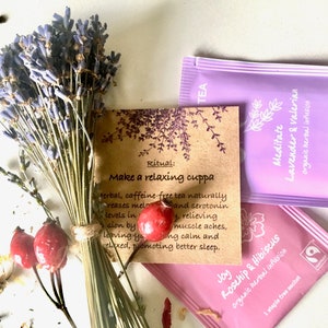 May include: A close-up of three tea bags with lavender and rosehip flavors. The tea bags are on a white surface with dried lavender flowers and rose hips. The tea bags are labeled with the text "Meditate Lavender & Valerian", "Joy Rosehip & Hibiscus", and "Ritual: Make a relaxing cuppa".