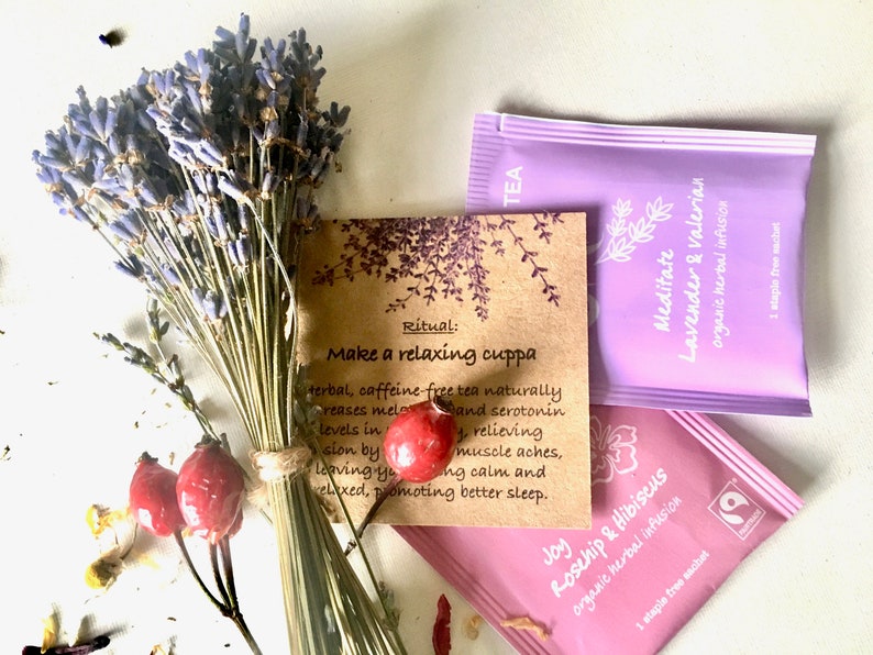 May include: A close-up of three tea bags with lavender and rosehip flavors. The tea bags are on a white surface with dried lavender flowers and rose hips. The tea bags are labeled with the text "Meditate Lavender & Valerian", "Joy Rosehip & Hibiscus", and "Ritual: Make a relaxing cuppa".