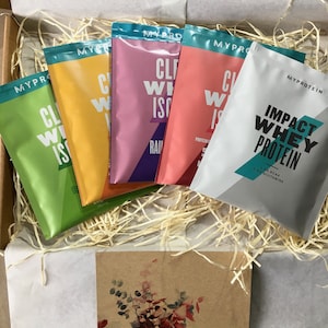 May include: A selection of Myprotein protein powder sachets in a box. The sachets are in various colours, including green, yellow, pink, and white. The box also contains decorative straw and a card with the text "Especially for you".