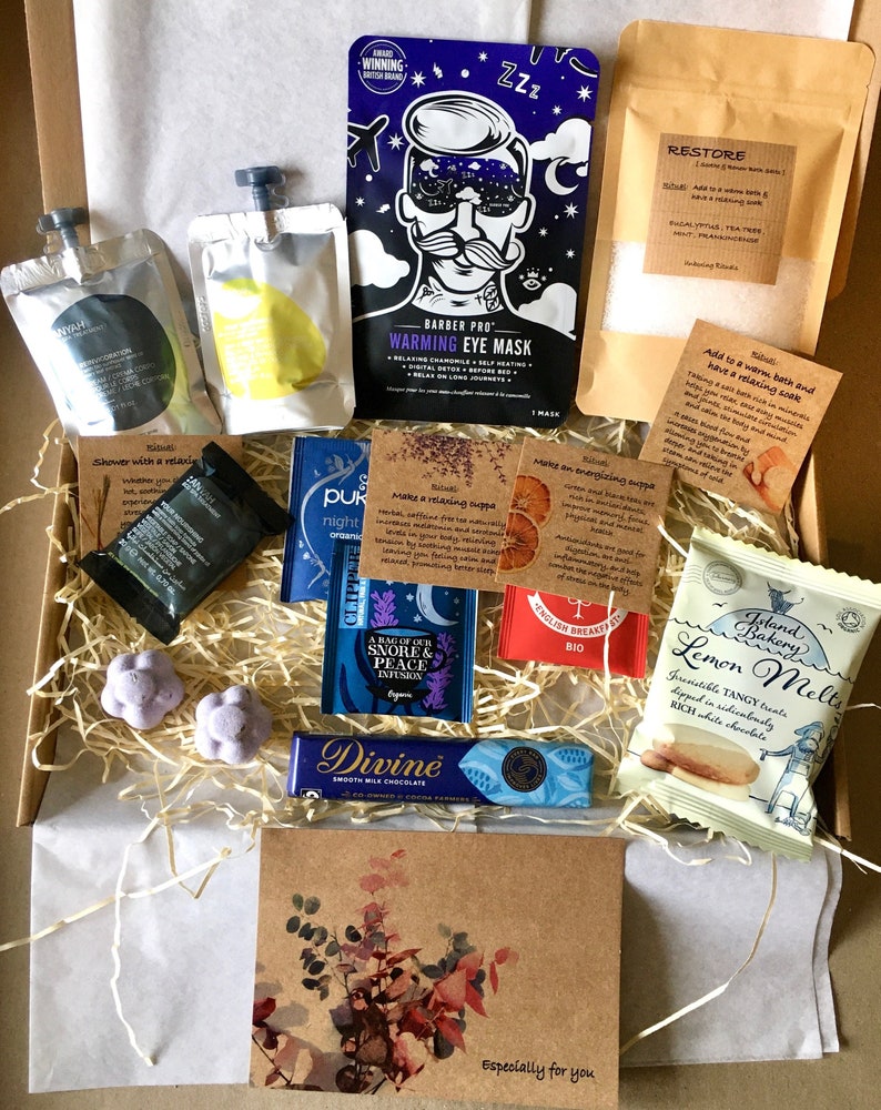 May include: A gift box filled with various self-care items, including bath salts, tea bags, chocolate, and a sleep mask. The box is lined with brown paper and straw. The text on the box reads "Especially for you".
