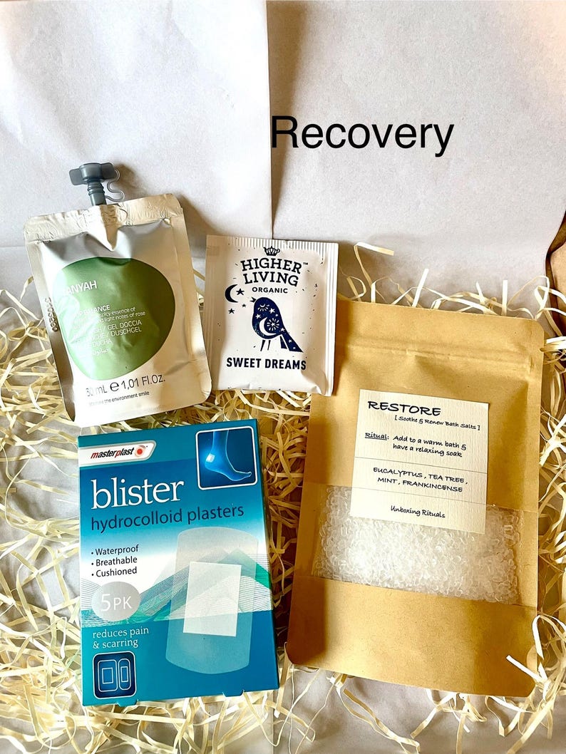 May include: A self-care gift set containing blister plasters, shower gel, bath salts, and tea. The box is filled with straw. The packaging includes the words "Recovery", "Sweet Dreams", and "Restore".