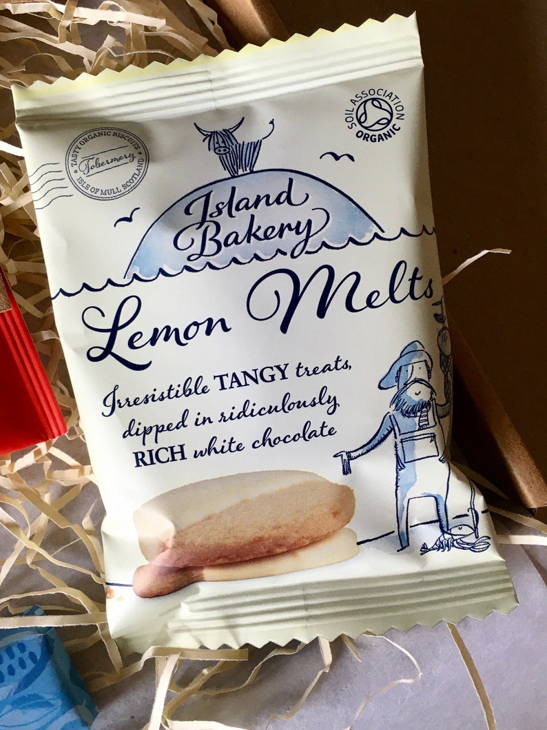 May include: A white and blue package of Island Bakery Lemon Melts. The package features a cartoon illustration of a cow on a hill with the text "Island Bakery Lemon Melts". The text "Irresistible TANGY treats, dipped in ridiculously RICH white chocolate" is also on the package.