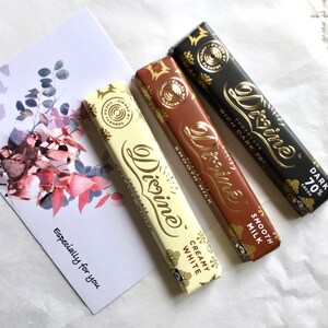 May include: Three Divine chocolate bars, one white, one milk chocolate, and one dark chocolate. The white chocolate bar says "Creamy White", the milk chocolate bar says "Smooth Milk", and the dark chocolate bar says "Rich Dark 70% Cocoa".