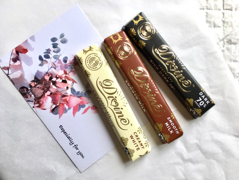 May include: Three Divine chocolate bars, one white, one milk chocolate, and one dark chocolate. The white chocolate bar says "Creamy White", the milk chocolate bar says "Smooth Milk", and the dark chocolate bar says "Rich Dark 70% Cocoa".