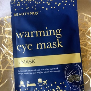 May include: A blue and gold package for a self-warming eye mask. The package features the text "warming eye mask" and "Relaxing Chamomile self warming eye mask".