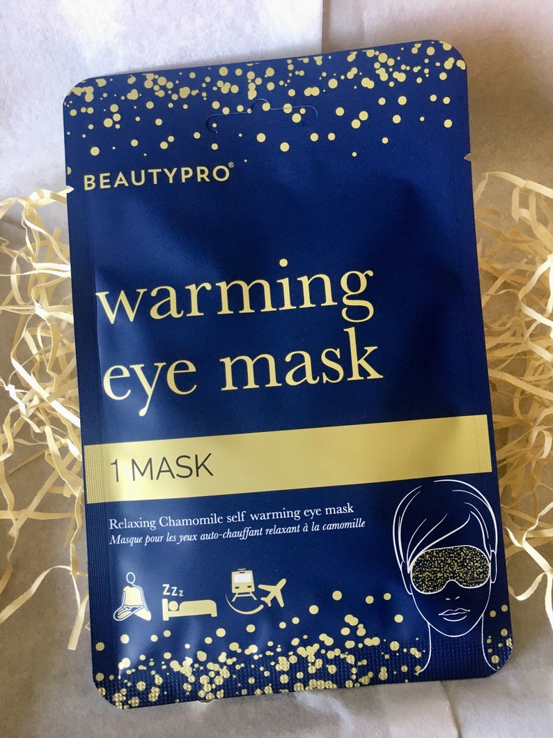 May include: A blue and gold package for a self-warming eye mask. The package features the text "warming eye mask" and "Relaxing Chamomile self warming eye mask".