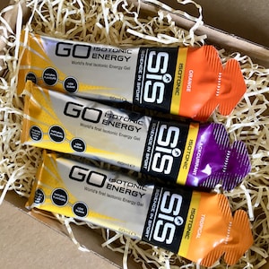 May include: Three 60ml SiS GO Isotonic Energy gel sachets in orange, blackcurrant, and tropical flavours. Each silver, black, and coloured foil packet features the text GO ISOTONIC ENERGY, Science in Sport, and labels for natural flavours and low sugar.