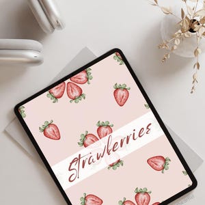 May include: A digital tablet displaying a seamless watercolor pattern of red strawberries on a pink background. The text "Strawberries" is written in white on a white banner across the screen. The text "@teodoratheartist" is in the bottom right corner of the screen.