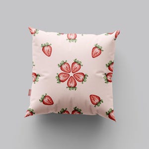 May include: A pink throw pillow with a repeating pattern of red strawberries. The strawberries are arranged in a circular pattern with the points of the strawberries facing outward.