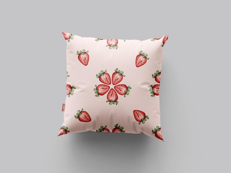 May include: A pink throw pillow with a repeating pattern of red strawberries. The strawberries are arranged in a circular pattern with the points of the strawberries facing outward.