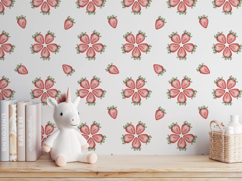 May include: A white stuffed unicorn toy sits in front of a white wall with a pink and green strawberry pattern. The wall is covered in a repeating pattern of strawberries.