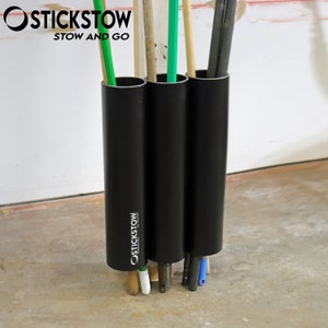 May include: Black PVC pipe holder with three compartments for storing brooms, mops, or other long handled tools. The holder is labeled "Stickstow Stow and Go".