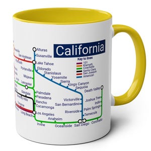 May include: A white ceramic mug with a yellow rim features a map of California with major cities and transportation lines. The map includes a key to lines with different colors representing different transportation routes. The text "California" is printed in black at the top of the mug.