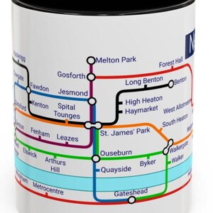 Puede incluir: Taza de cer&aacute;mica blanca con borde negro que presenta un mapa colorido del sistema de metro de Newcastle upon Tyne. El mapa incluye nombres de estaciones como Gosforth, Jesmond, Haymarket y Byker.