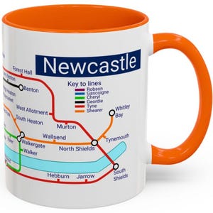 Puede incluir: Taza de cer&aacute;mica blanca con un mapa colorido del sistema de metro de Newcastle. La taza tiene un borde y un asa naranja. El mapa incluye los nombres de las estaciones y las diferentes l&iacute;neas. El texto "Newcastle" est&aacute; impreso en azul en la parte superior de la taza.