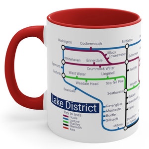 May include: White ceramic mug with a red rim and handle. The mug features a map of the Lake District in England, with the names of towns and cities, and a key to the different colored lines on the map. The text "Lake District" is printed in black on the mug.