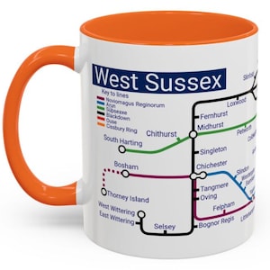 Könnte beinhalten: Eine weiße Keramiktasse mit orangefarbenem Henkel. Die Tasse zeigt eine Karte von West Sussex mit einem Schlüssel für Linien und Bahnhöfe. Die Karte ist im U-Bahn-Stil.
