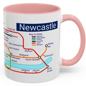 Puede incluir: Taza de cer&aacute;mica blanca con borde y asa de color rosa. La taza presenta un mapa del sistema de metro de Newcastle con el t&iacute;tulo "Newcastle" en texto azul. El mapa incluye los nombres de las estaciones y las l&iacute;neas, con una clave de l&iacute;neas que muestra los colores de cada l&iacute;nea.