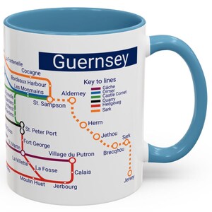 Puede incluir: Taza de cer&aacute;mica blanca con asa azul. La taza presenta un mapa de las Islas del Canal con el texto "Guernsey" en azul en la parte superior. El mapa muestra las islas de Guernsey, Alderney, Sark, Herm y Jersey. El mapa tambi&eacute;n incluye una clave de l&iacute;neas con diferentes l&iacute;neas de colores que representan diferentes rutas de transporte.