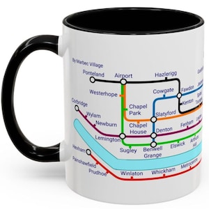 Puede incluir: Taza de cer&aacute;mica blanca con asa y borde negros. La taza presenta un mapa colorido del sistema de metro de Tyne and Wear en el Reino Unido. El mapa incluye nombres de estaciones como Airport, Westerhope y Metrocentre.