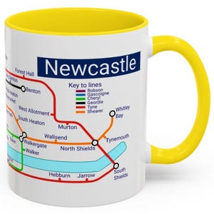 Puede incluir: Taza de cer&aacute;mica blanca con borde y asa amarillos. La taza presenta un mapa del sistema de metro de Newcastle con el texto "Newcastle" y "Key to lines" impreso en la parte delantera.