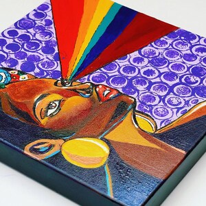 May include: Square canvas art featuring a stylized portrait of a person with brown skin, adorned with colorful earrings and a floral headpiece. A rainbow emanates from the person's eye, set against a purple bubble pattern background.