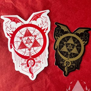 The Red sticker and Mirror Gold sticker are displayed on a red paper background. The Red sticker has a white background. The Mirror Gold sticker looks more matt here as it has less light. Icewreath's shop logo is placed in the corner.
