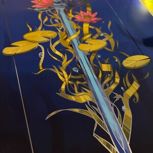 May include: A blue sword with a silver blade is surrounded by gold vines and pink water lilies on a dark blue background.