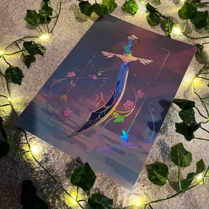May include: A holographic print of a sword with a blue blade and gold accents. The sword is surrounded by pink and green flowers and butterflies. The background is a gradient of purple, pink, and blue.