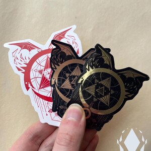 A hand holds the three variants of the sticker, showing the differences between them. The Red sticker has a white background. The Brushed Metal has a line-like reflective quality. Icewreath's shop logo is placed in the corner.