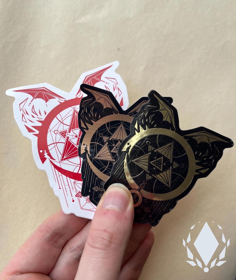 A hand holds the three variants of the sticker, showing the differences between them. The Red sticker has a white background. The Brushed Metal has a line-like reflective quality. Icewreath's shop logo is placed in the corner.