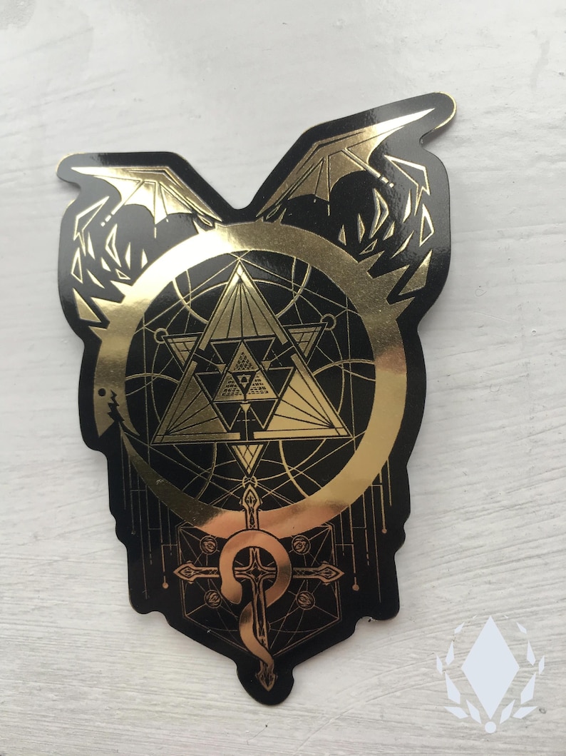The Mirror Gold sticker sits at a slight angle on a white painted background, a light shining on the golden parts of the sticker, showing their reflective golden quality. Icewreath's shop logo is placed in the corner.