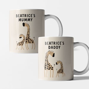 Puede incluir: Dos tazas de cerámica blanca con asas negras. Las tazas tienen un fondo beige con una ilustración de dibujos animados de dos jirafas. El texto "Beatrice's Mummy" y "Beatrice's Daddy" está impreso en negro en las tazas.