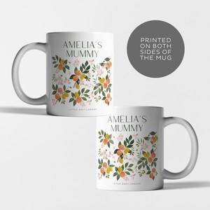 May include: White ceramic mug with a floral design featuring orange blossoms, lemons, and bees. The mug has the text "Amelia's Mummy" printed on it.