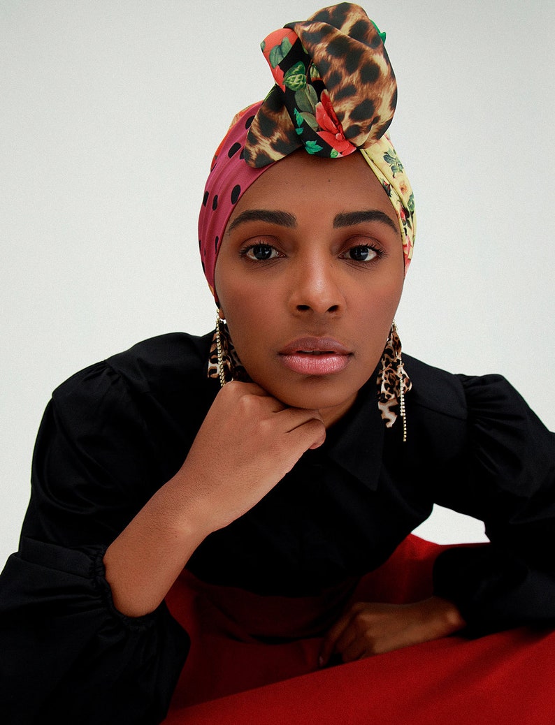 May include: A woman wearing a black shirt and red pants with a colorful patterned headscarf and gold earrings.