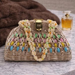 May include: A woven straw handbag with a gold clasp and colorful accents. The bag features a pattern of pastel-colored beads and a beaded strap. A bottle of perfume sits in the background.