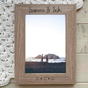 May include: A wooden picture frame with a photo of a couple holding hands on a beach. The frame is engraved with the names "Sammie & Josh" and the date "31 ♥ 12 ♥ 22".